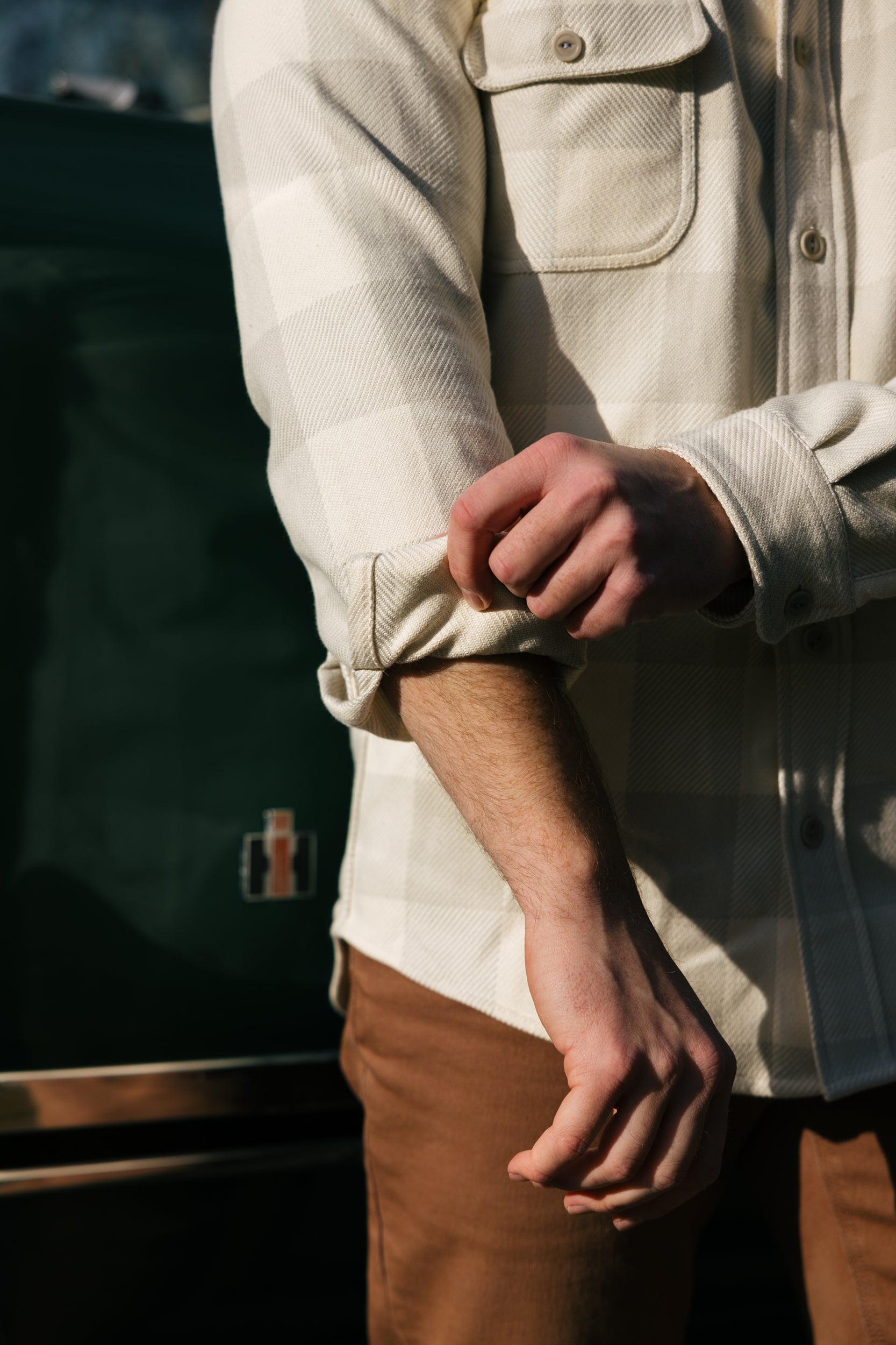 Man rollin up the sleeve of a tan plaid Six Season flannel shirt by Warren.