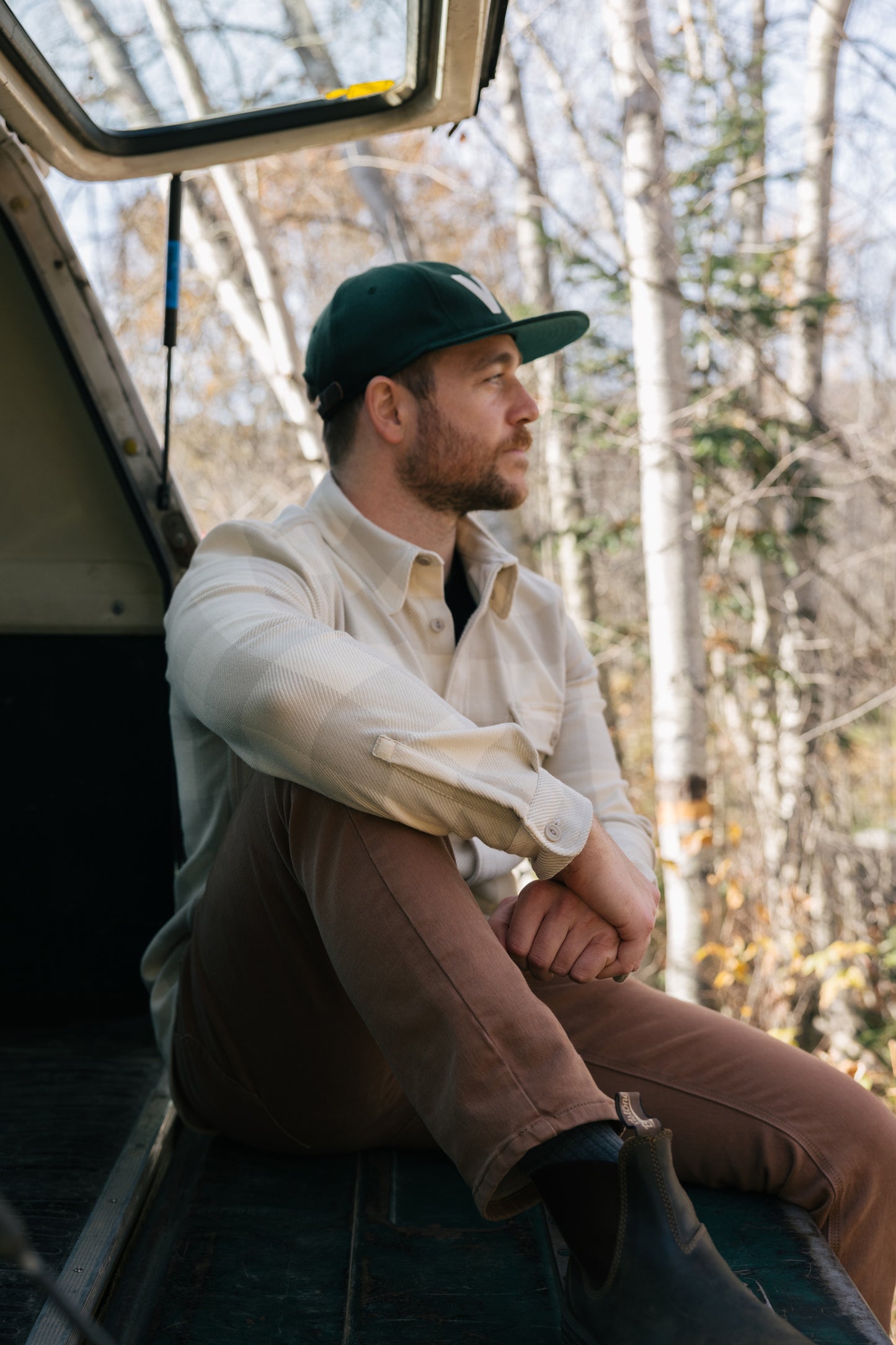 Man wearing a tan plaid Six Season flannel shirt by Warren as he sits in the back of a truck.