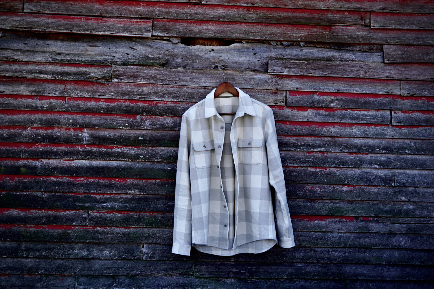 Warren Six Season flannel shirt in Birch, sitting on a hanger on the side of a barn. 