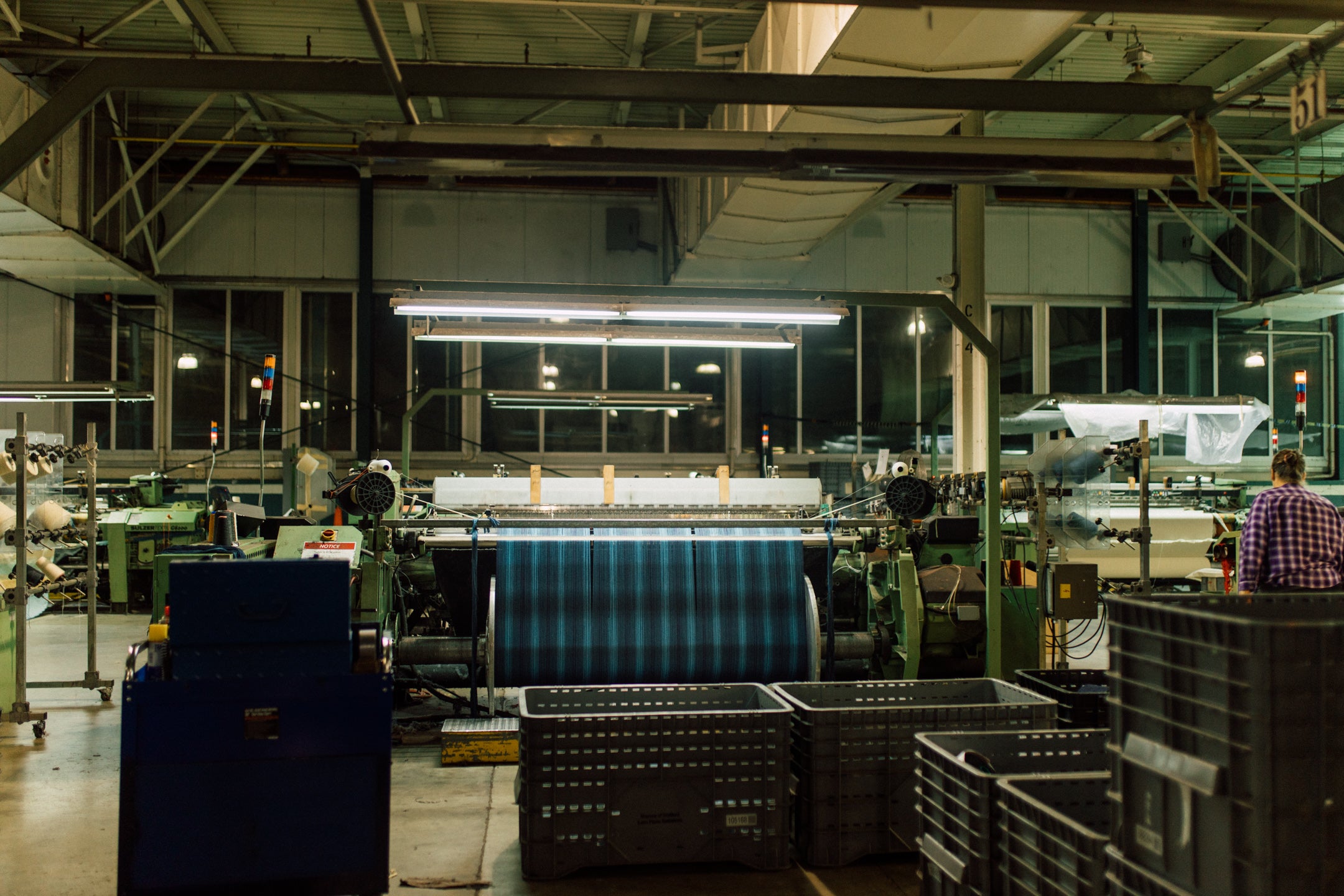 A weaving machine inside a textile mill with a worker.